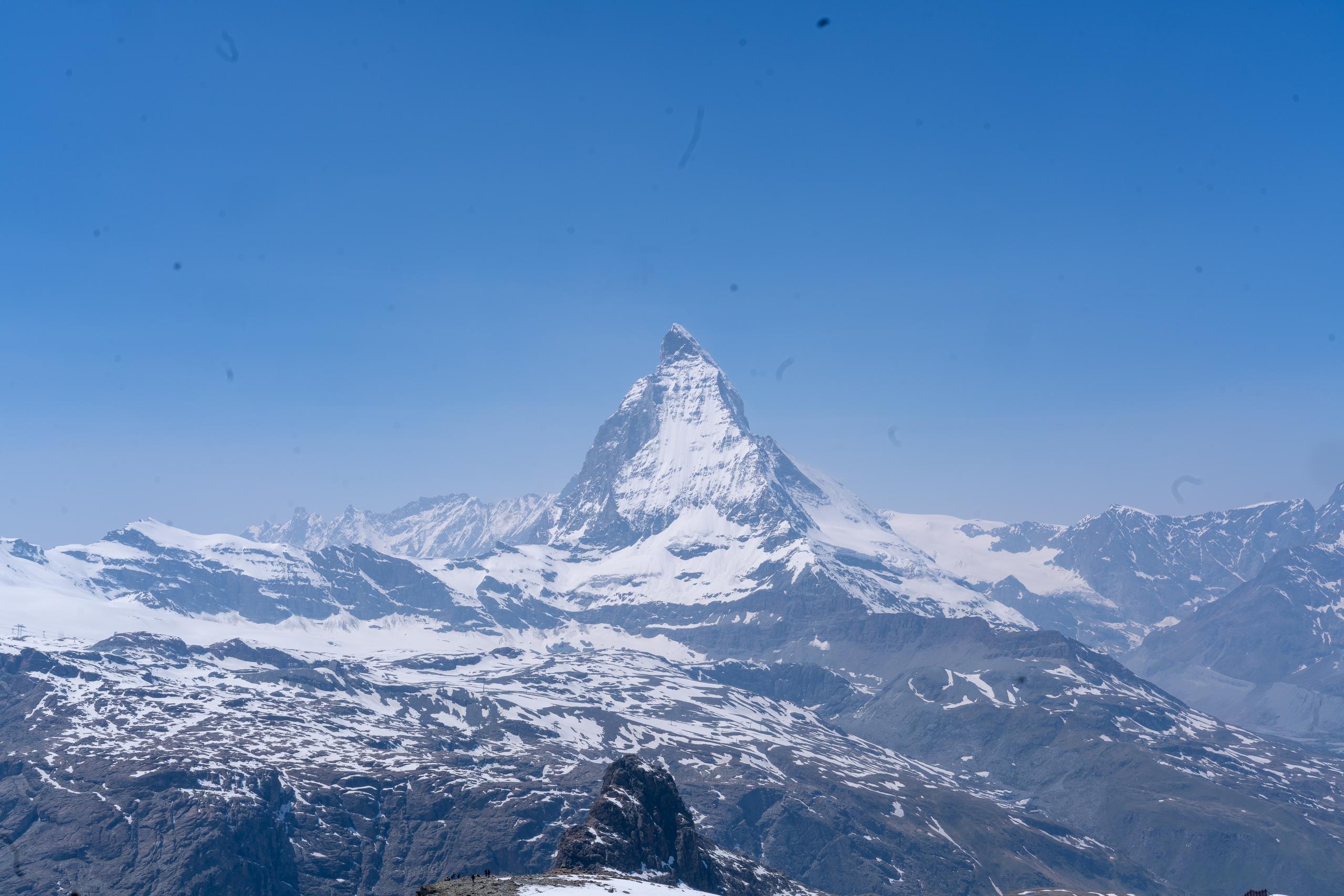 An isolated pyramid-shaped snow peak stands in the center of the frame. The mountain is steep, the rock walls are exposed and covered with snow; below the peak are vast glaciers and snow-covered rock ridges, and the sky is pure deep blue.