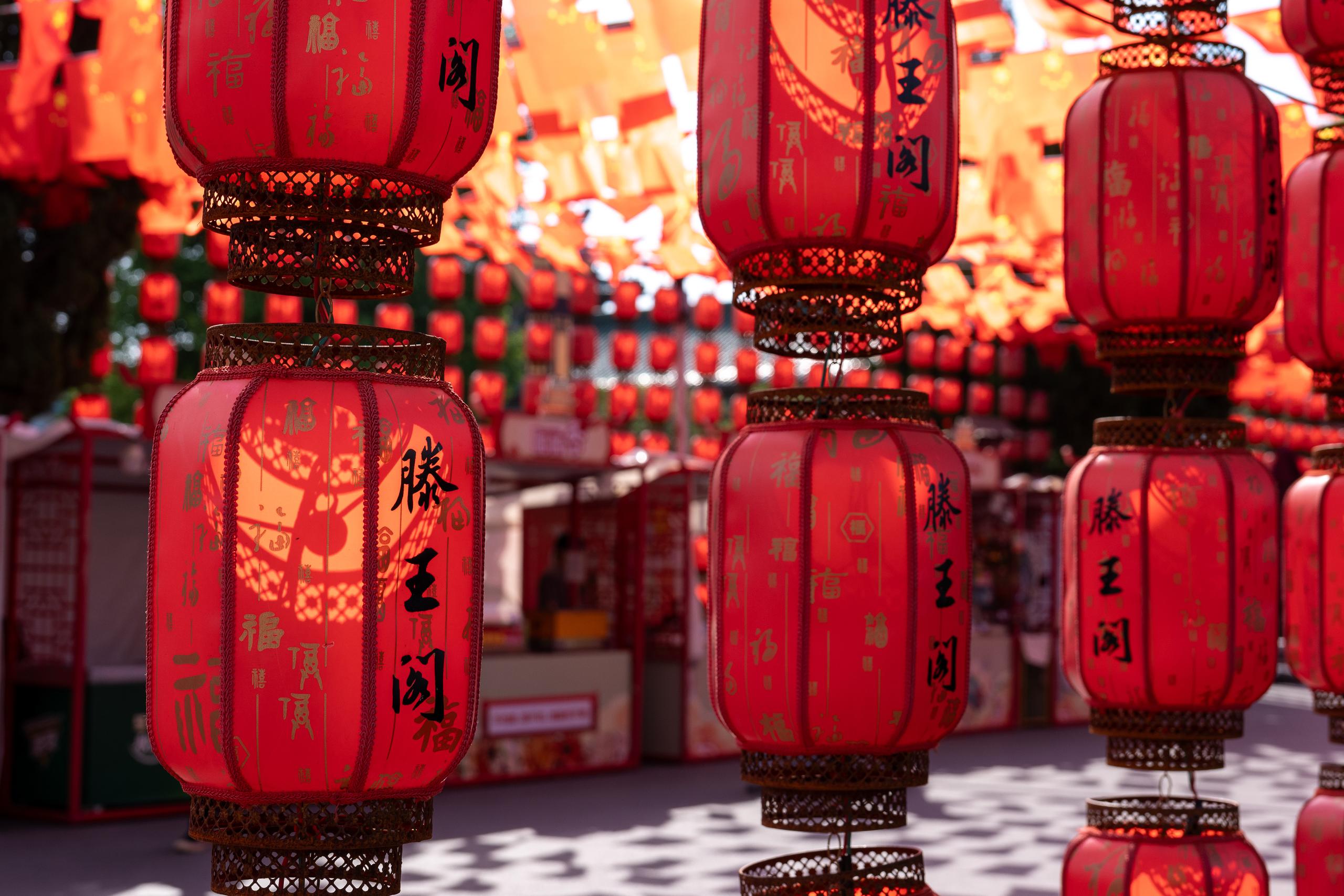 Hundreds of red lanterns are hung densely in the frame. A few lanterns are very close in the foreground. The surface of the lanterns has golden patterns and black calligraphy, and the upper and lower edges are decorated with golden hollow cloud patterns. In the background, more lanterns are connected together and blurred into red spots.