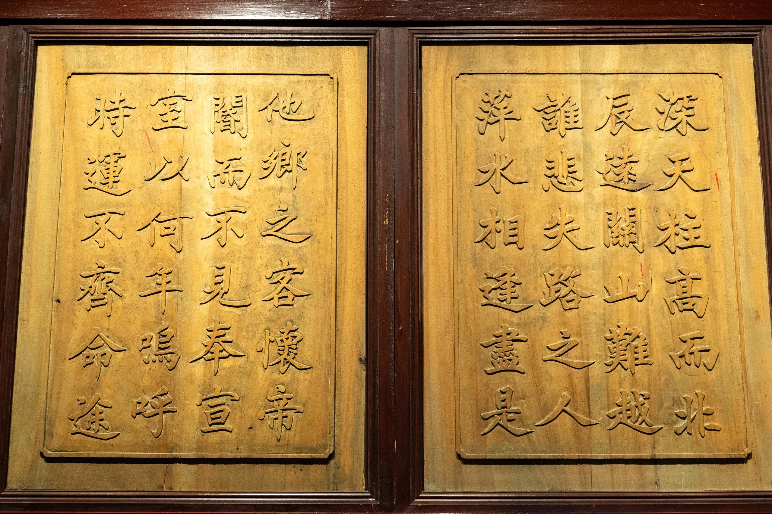 Two side-by-side light yellow woodcut frame panels are mounted in dark wooden frames. Each panel is lined with multiple columns of incised Chinese calligraphy. The layout has a thin border, and wood grain and wear marks can be seen on the surface of the panels.